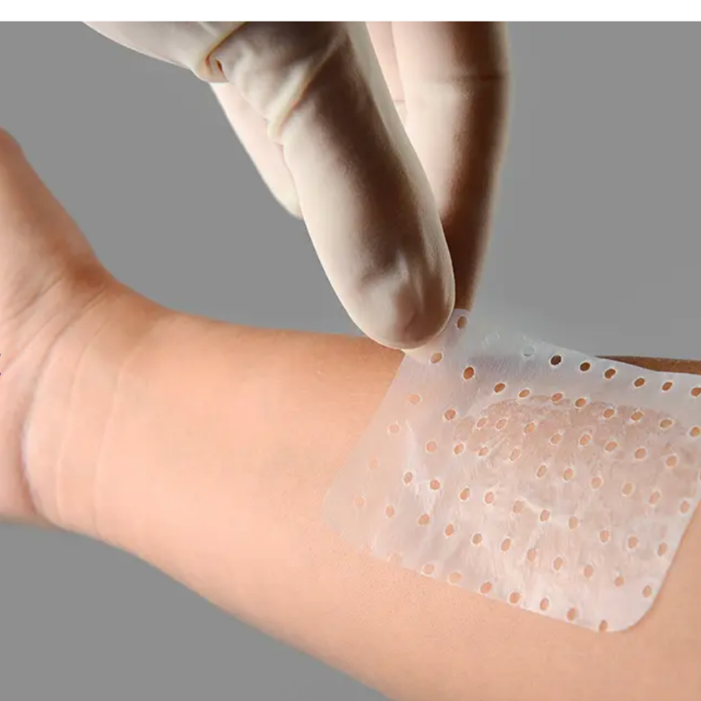 Person applying a transparent adhesive patch to their arm with a gloved hand.